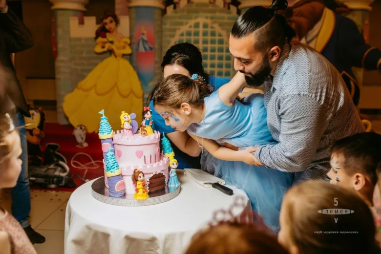 Дівчина дмухає свічки на торті з принцесами для дня народження