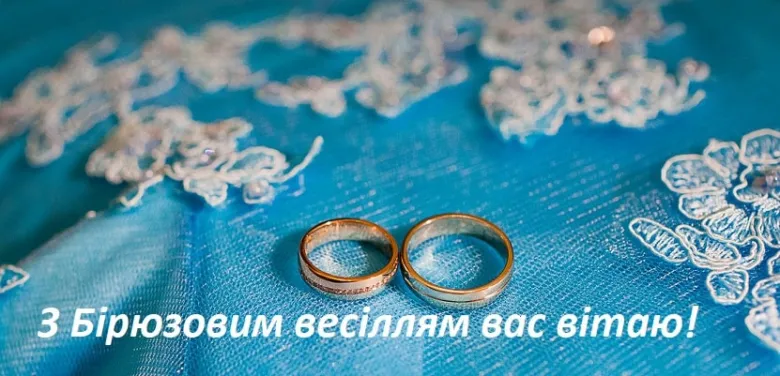 Два золоті кільця на блакитній тканині з вітанням до бірюзового весілля.