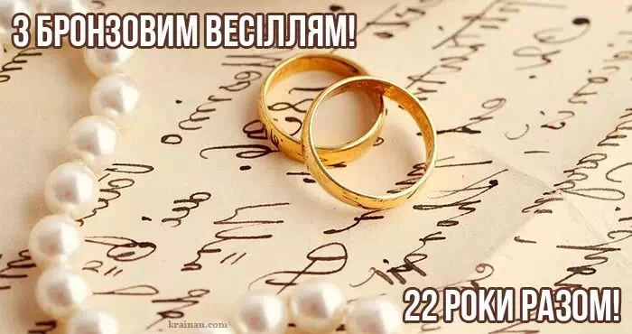 Золоті обручки та перлини на фоні рукопису для бронзового весілля.